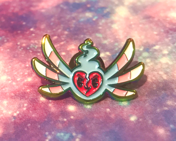 A textured enamel pin with raised iridescent metal outline around recessed enamel, making a four colour version of the LauraKBuzz logo, a smiling read heart surrounded by blue flames and three pairs of narrow wings which change colour out from the centre in trans pride colours from blue to pink then white